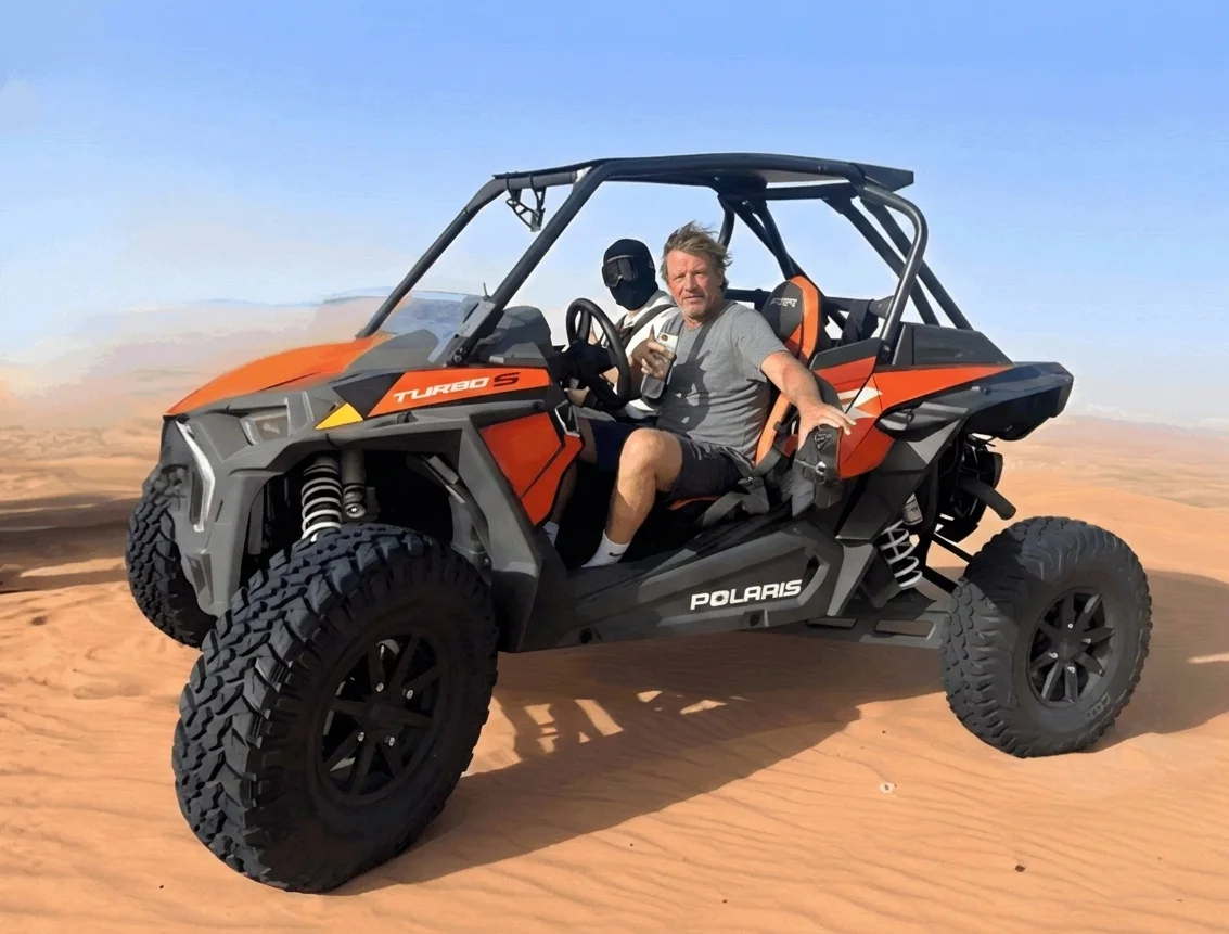 Two seater dune buggy exploring open red sand dunes in Lahbab desert Dubai with safety helmets and guided convoy ride under clear sky