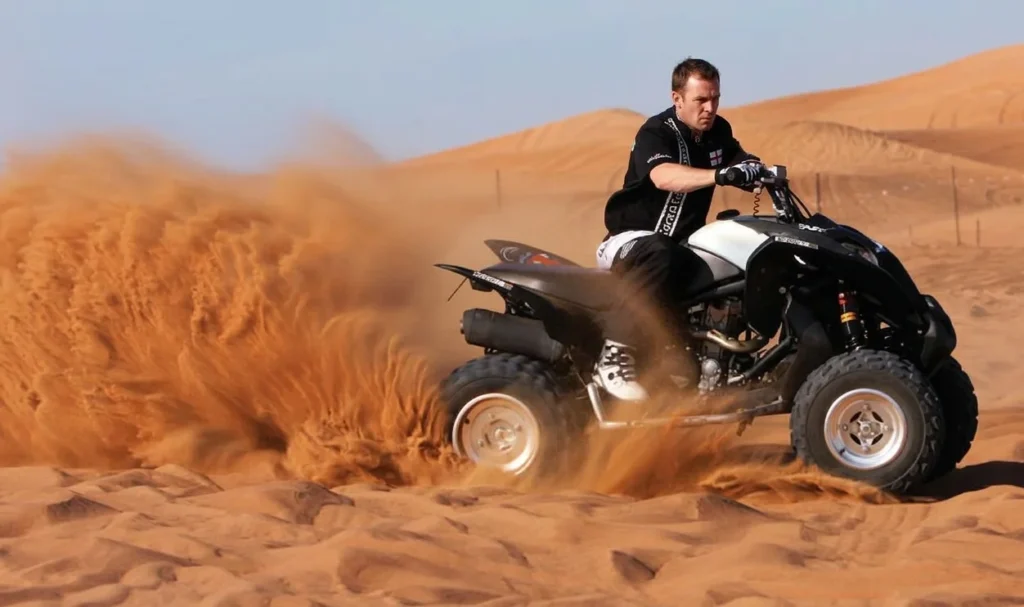 Tourists riding quad bikes across the red sand dunes of Dubai desert during an adventure tour while learning safe riding techniques with guide support.