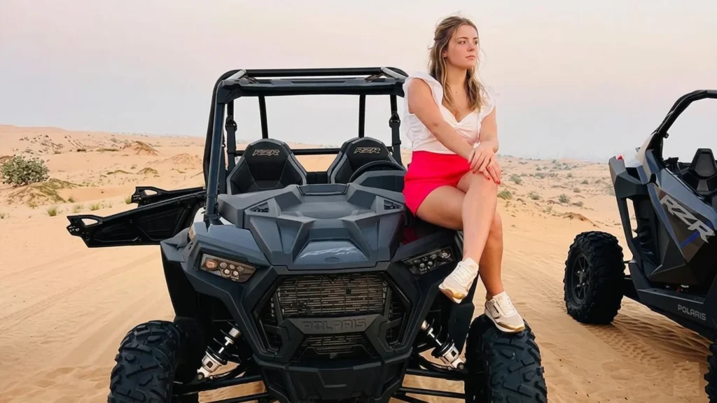 Beginner driving a dune buggy across Dubai desert dunes with guide leading ahead, showcasing safe first time off road adventure experience